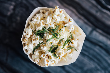 Top view of rosemary popcorn in paper bag on top marble table.
