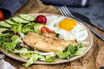 Served healthy breakfast with fried eggs and vegetable Top view of plate of tasty fried eggs with chicken and avocado with colorful vegetable salad placed next to knife and fork on kitchen table