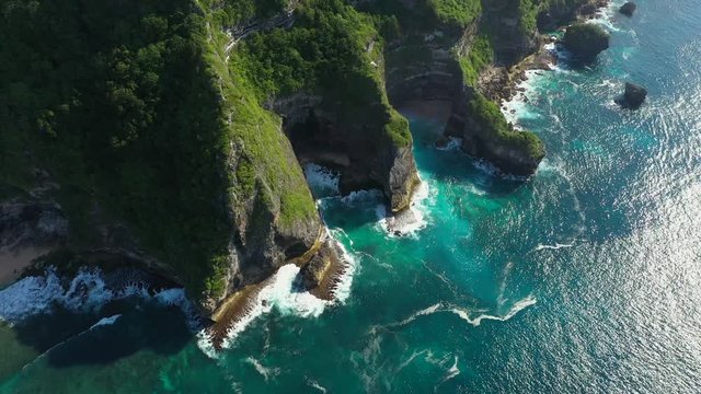 Bali - Bukit peninsula. Aerial footage of transparent turquoise ocean and rocky cliffs, covered with tropical trees.