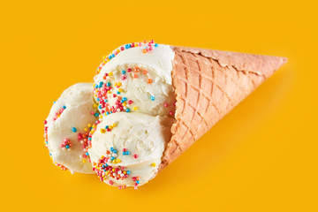 ice cream balls with colored sugar sprinkles in a Waffle Cone on a yellow Background. Vanilla ice cream in a waffle cone.
