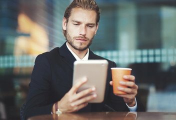     Handsome businessman enjoying a cup of coffee and looking his tablet