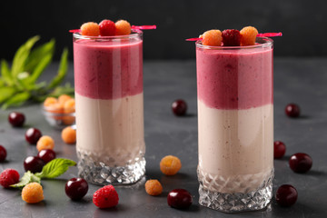 Smoothies with berries of yellow raspberry and cherry in glasses on a dark background