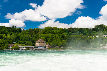 Fototapeta na wymiar Beautiful, turquoise Rhine river flowing from a waterfall in northern Switzerland. Waterfall on the river Rhine. Visible boat and old castle on a small island.