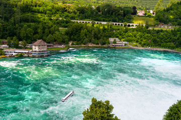 Beautiful, turquoise Rhine river flowing from a waterfall in northern Switzerland. Waterfall on the river Rhine. Visible boat and old castle on a small island.
