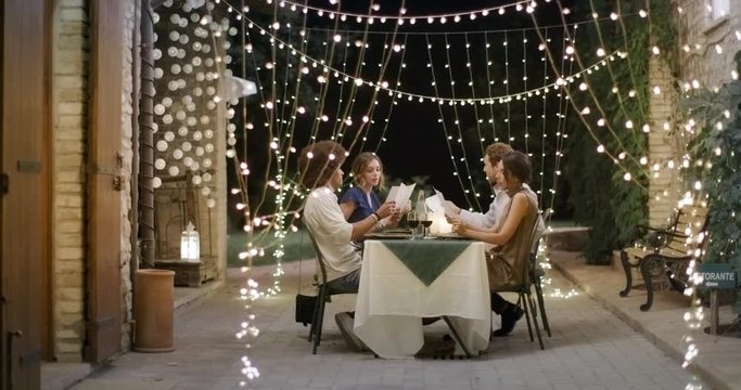 Four people, two couples happy talking and eating during a romantic gourmet dinner or lunch.Approaching wide shot. Friends italian trip in Umbria.4k slow motion