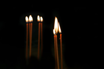 Fototapeta premium Candle flames on a black background. Burning prayer candles in the church.