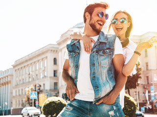 Smiling beautiful girl and her handsome boyfriend. Woman in casual summer dress.Man in jeans clothes. Happy cheerful family. Female having fun on the street background.Shows peace sign in sunglasses