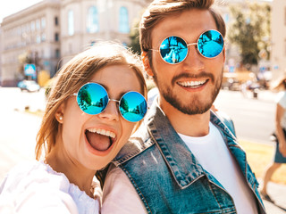 Smiling beautiful girl and her handsome boyfriend in casual summer clothes.Happy family taking selfie self portrait of themselves on smartphone camera in sunglasses.Having fun on the street background