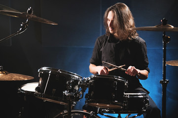 Portrait of a long-haired drummer with chopsticks in his hands sitting behind a drum set. Low key. Concepts of the creative freedom of the millenial generation