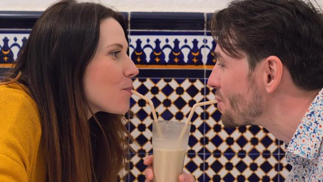 Close-up shot of young loving couple sipping horchata with straws from one glass