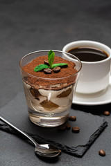 Classic tiramisu dessert in a glass on stone serving board and cup of coffee on dark concrete background