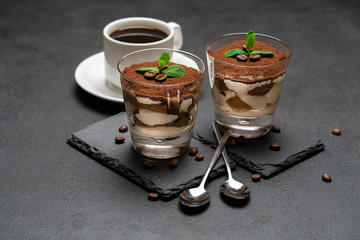 Classic tiramisu dessert in a glass on stone serving board and cup of coffee on dark concrete...