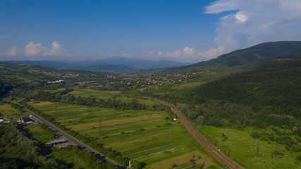 Aerial view of the Carpathian mountains. Natural background with geometric pattern - beige and red rectangles of the fields and roofs and lines of roads and trees. Zakarpattia, Ukraine.