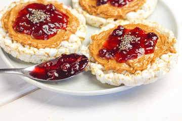 crunchy natural peanut butter strawberry jam jelly sandwich with chia seeds on rice cake bread. Proper nutrition diet vegetarian breakfast on plate next to knife with peanut butter