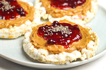 crunchy natural peanut butter strawberry jam jelly sandwich with chia seeds on rice cake bread. Proper nutrition diet vegetarian breakfast on plate next to knife with peanut butter