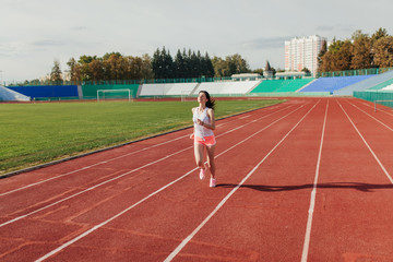 Fototapeta premium Athletic young woman in sportswear sprinting on running track stadium at sunset