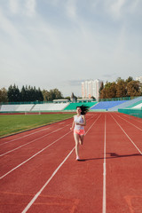 beautiful young woman in pink shorts and tank to exercise jogging and running on athletic track on stadium at sunrise