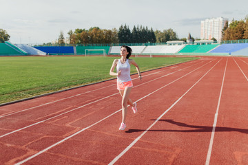 Young woman in pink shorts and tank to running during sunny morning on stadium track