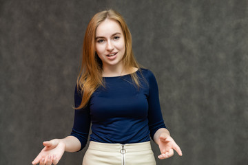 Portrait of a knee-high beautiful pretty red-haired woman girl in a blue jacket with a light skirt on a gray background in the studio. Smiles, shows emotions, talks, spreads his hands.