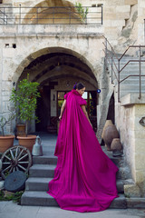Naklejka premium girl in a long purple dress stands at the entrance to the rock