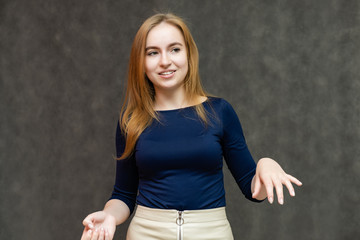 Portrait of a knee-high beautiful pretty red-haired woman girl in a blue jacket with a light skirt on a gray background in the studio. Smiles, shows emotions, talks, spreads his hands.