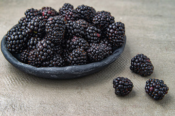 Blackberries ripe in a gray clay bowl on a gray background. Organic , juicy and healthy berries. Scandinavian style.