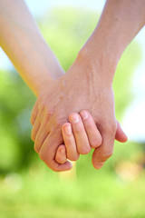Couple holding hands and walking in sunny summer weather. Concept of close and trusting relationships. Happy young family
