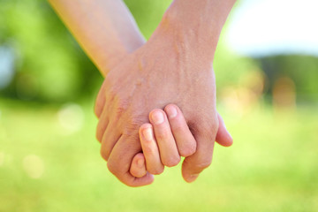 Couple holding hands and walking in sunny summer weather. Concept of close and trusting relationships. Happy young family