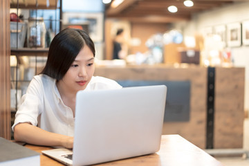 Young Asian woman working with a laptop in the coffee shop cafe office.