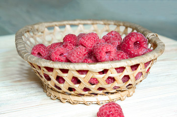 raspberries in a basket on a light wooden background