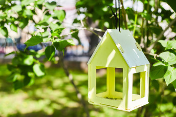 Obraz na płótnie Canvas Yellow bird house hanging from the tree and surrounded by lush foliage. Nest box on a green background with copy space
