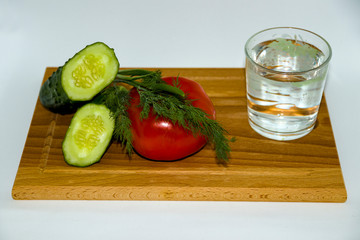 Fresh juicy tomato, green onion, glass of water, sliced cucumber, dill, salad, on wooden chopping Board on white background