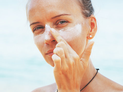 A Young Woman Applies Sunscreen To Her Face.