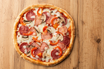 Top view of delicious Capricciosa Pizza on wooden table. Ingredients peeled tomato, cheese, ham, mushrooms, salami.