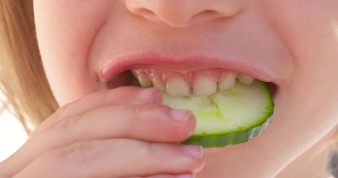 Close up, mouth of a child biting and chewing a fresh slice of cucumber