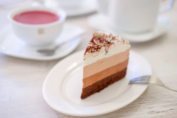 Piece of triple chocolate mousse cake on a white plate in cafe. Sweet dessert concept.