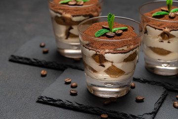 Classic tiramisu dessert in a glass on stone serving board on dark concrete background
