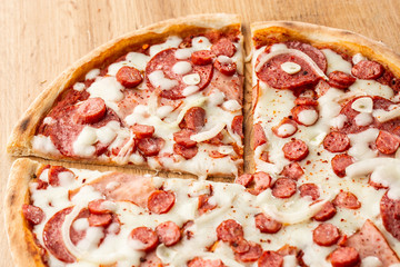 Top view of pizza with chili pepper , hot sausages, onion, ham, salami, garlic, tomatoes and cheese.