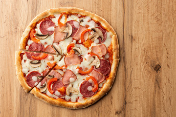 Top view of delicious Capricciosa Pizza on wooden table. Ingredients peeled tomato, cheese, ham, mushrooms, salami.