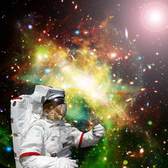 Astronaut gives thumbs-up against outer space, galaxies and stars. The elements of this image...