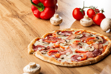 Top view of delicious Capricciosa Pizza on wooden table. Ingredients peeled tomato, cheese, ham, mushrooms, salami.