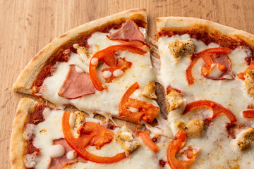 Flat lay with traditional Italian pizza with chicken, ham, cheese and tomatoes on wooden  back.