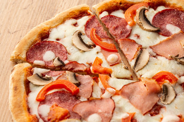 Top view of delicious Capricciosa Pizza on wooden table. Ingredients peeled tomato, cheese, ham, mushrooms, salami.