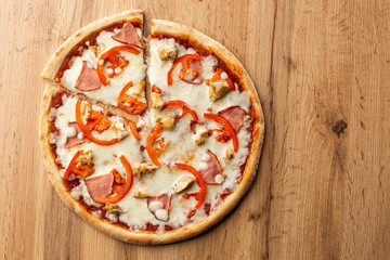 Flat lay with traditional Italian pizza with chicken, ham, cheese and tomatoes on wooden  back.