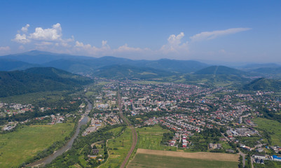 Aerial view of the Svalyava in Carpathian mountains. Natural background with geometric pattern - beige and red rectangles of the fields and roofs and lines of roads and trees. Zakarpattia, Ukraine.