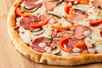 Top view of delicious Capricciosa Pizza on wooden table. Ingredients peeled tomato, cheese, ham, mushrooms, salami.