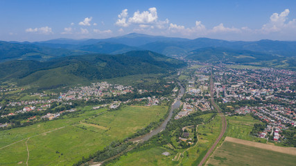 Fototapeta na wymiar Aerial view of the Svalyava in Carpathian mountains. Natural background with geometric pattern - beige and red rectangles of the fields and roofs and lines of roads and trees. Zakarpattia, Ukraine.
