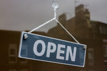 OPen sign hanging in a shop window at a diagonal angle reflecting british houses