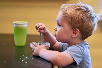 two-year-old boy is naughty and does not want to eat porrige with a spoon at the table in the kitchen