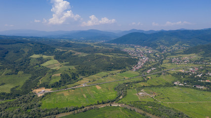 Fototapeta na wymiar Aerial view of the Carpathian mountains. Natural background with geometric pattern - beige and red rectangles of the fields and roofs and lines of roads and trees. Zakarpattia, Ukraine.